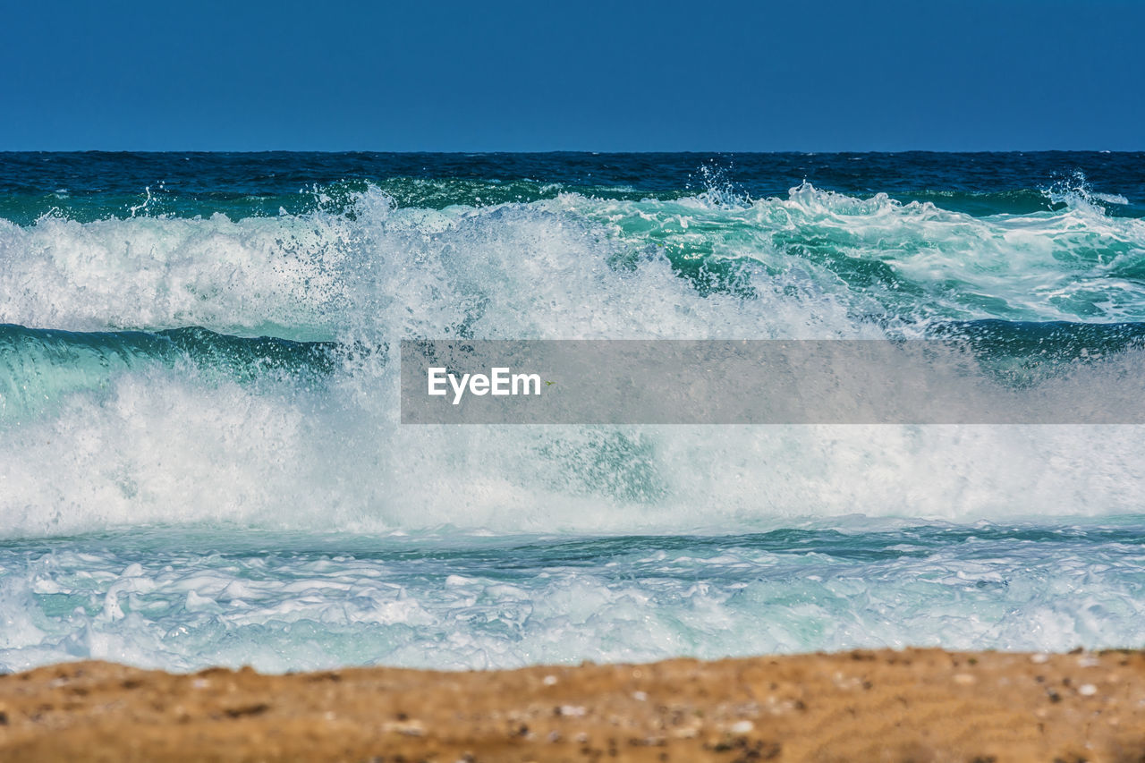 Waves splashing on shore against clear sky