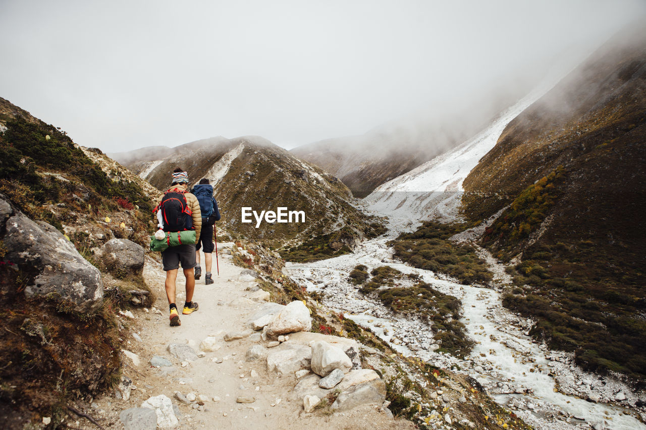 Rear view of friends with backpacks hiking at sagarmatha national park during foggy weather