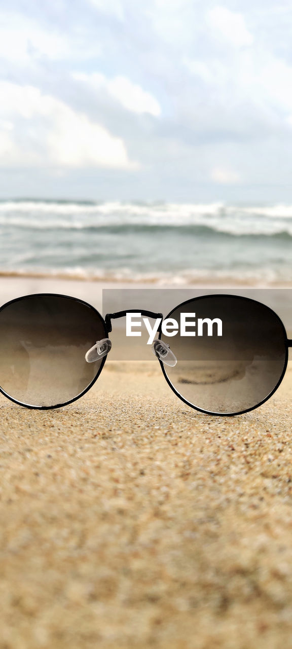 CLOSE-UP OF SUNGLASSES ON BEACH AGAINST SEA