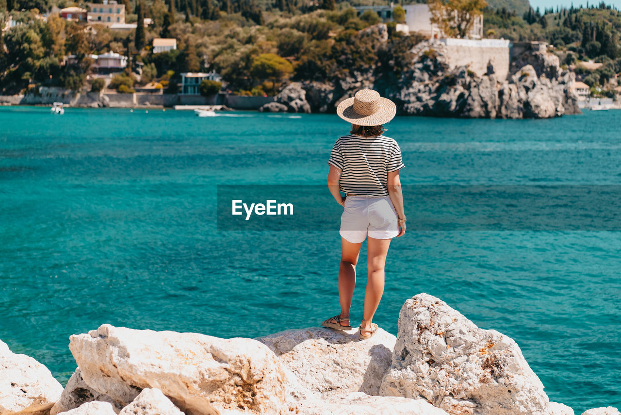 Rear view of woman standing on rock by sea