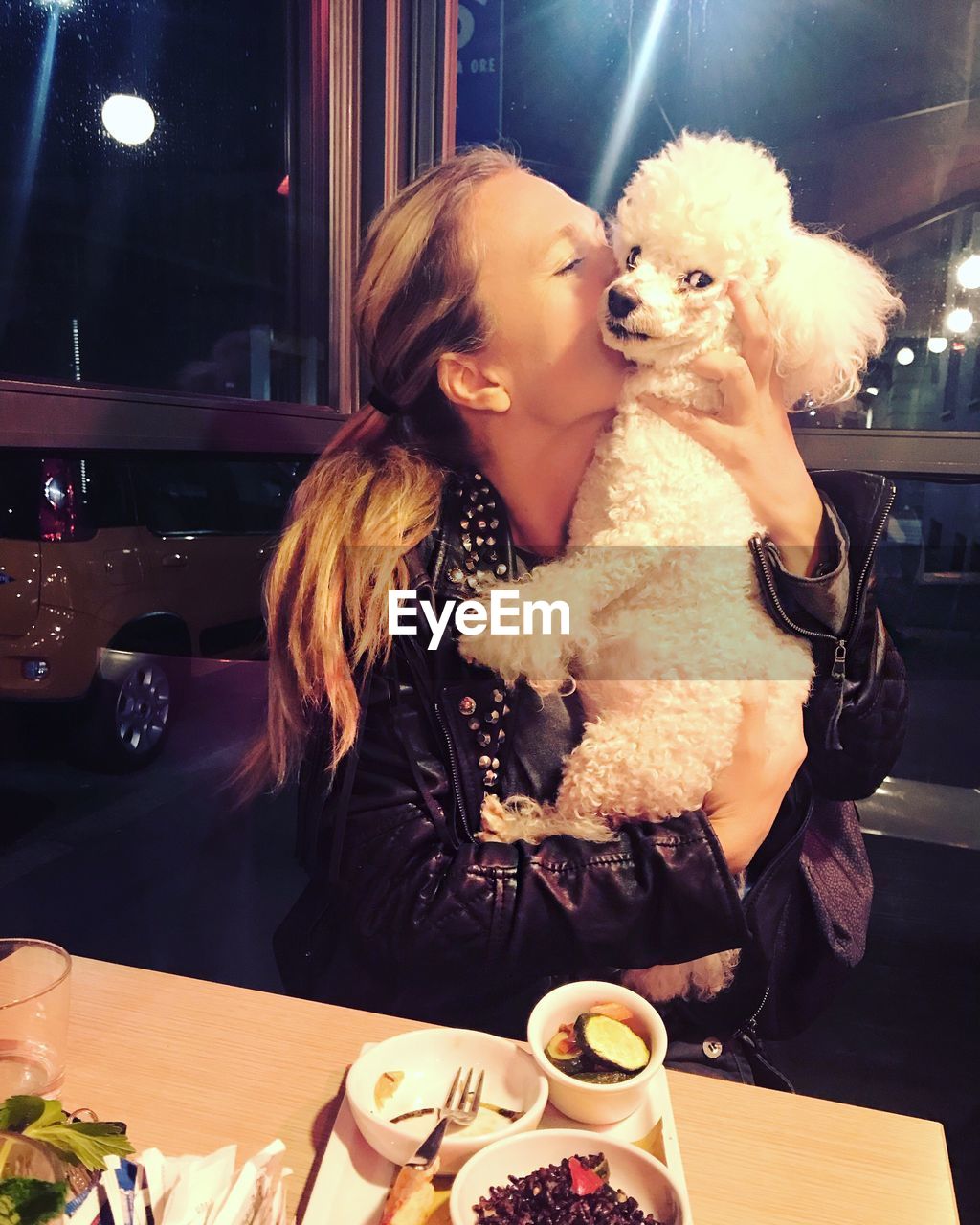 Young woman kissing dog while sitting at restaurant