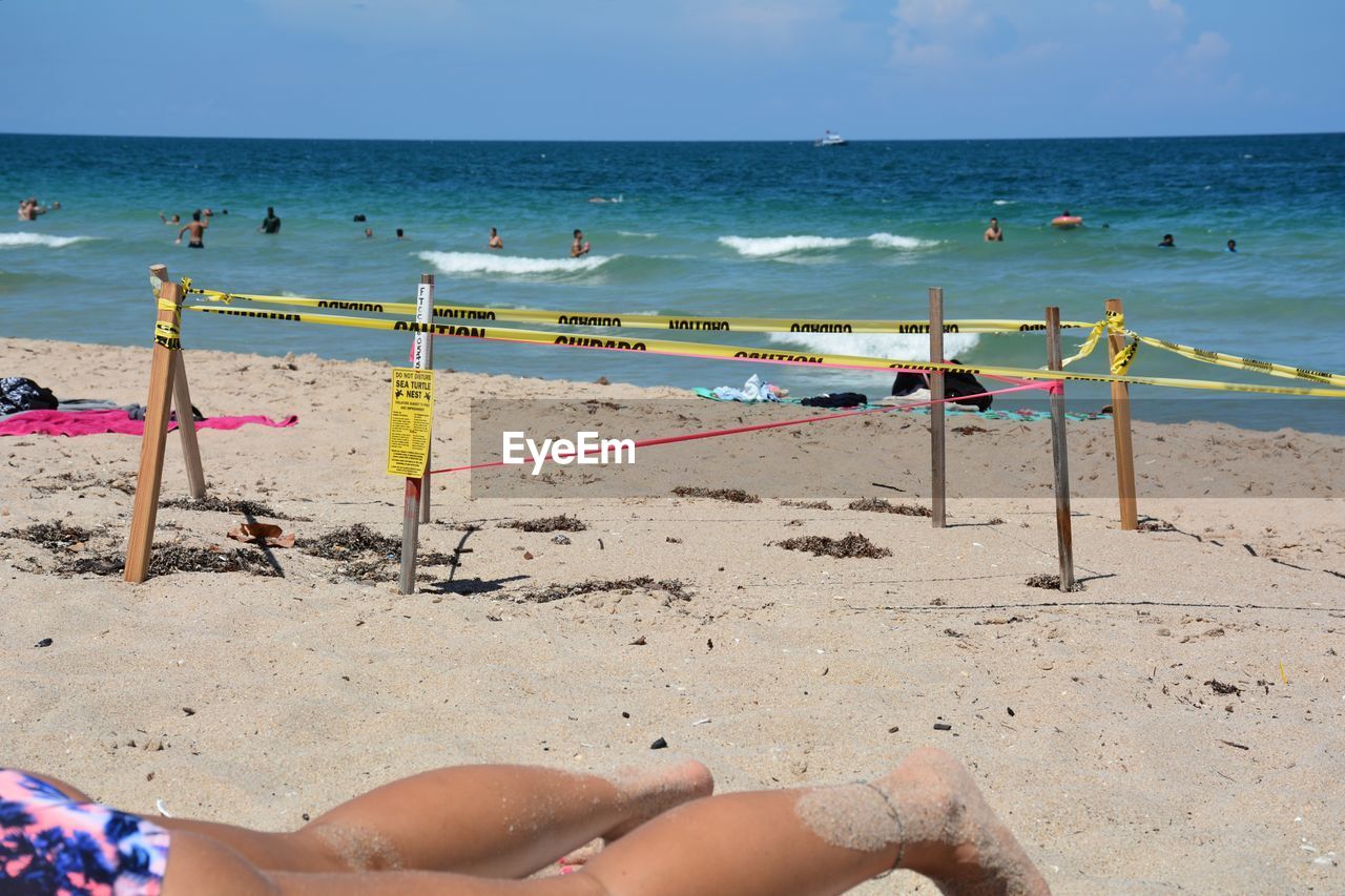 LOW SECTION OF PERSON ON BEACH BY SEA AGAINST SKY