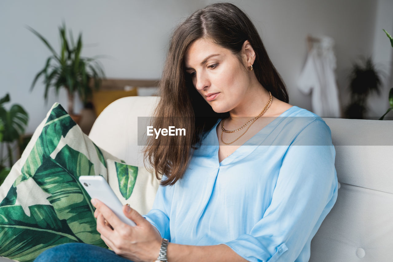 Young woman looking away while sitting on sofa at home