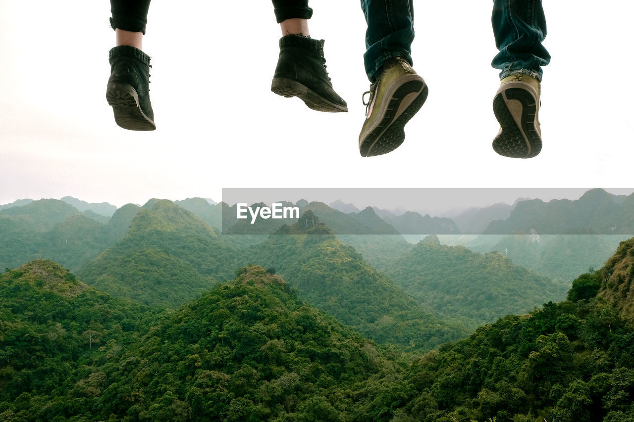 Low section of people over mountains against clear sky