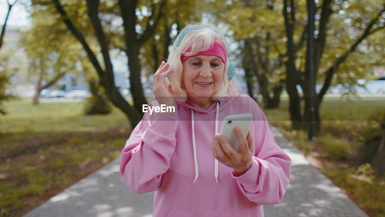 Senior woman using phone while listening music through headphones in park