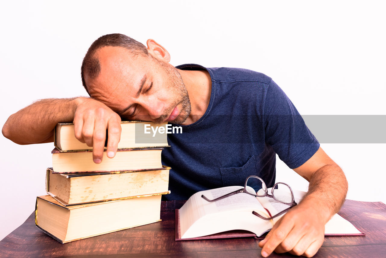 MIDSECTION OF MAN READING BOOK ON TABLE AGAINST GRAY BACKGROUND