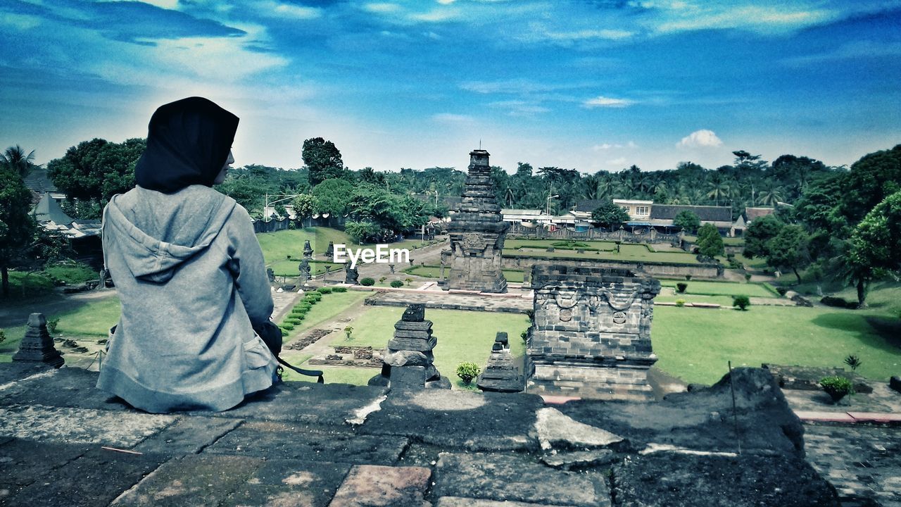 Rear view of woman sitting against penataran temple against sky