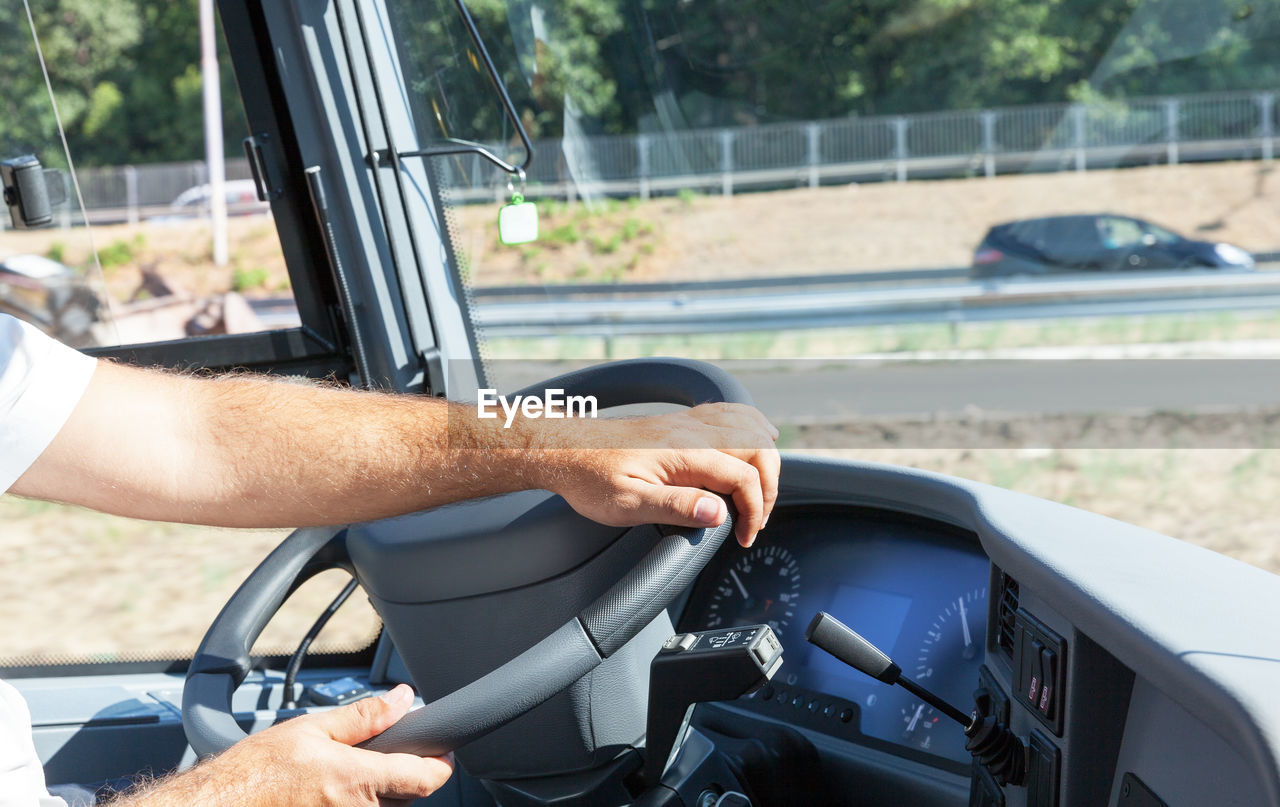 Cropped hands of man driving bus in city