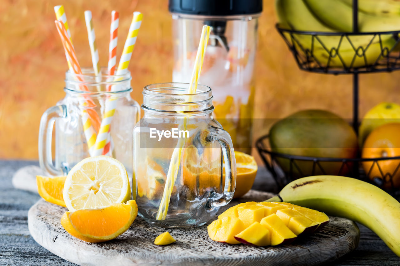 Empty jar mugs surrounded by fresh fruit to make a mango citrus smoothie.