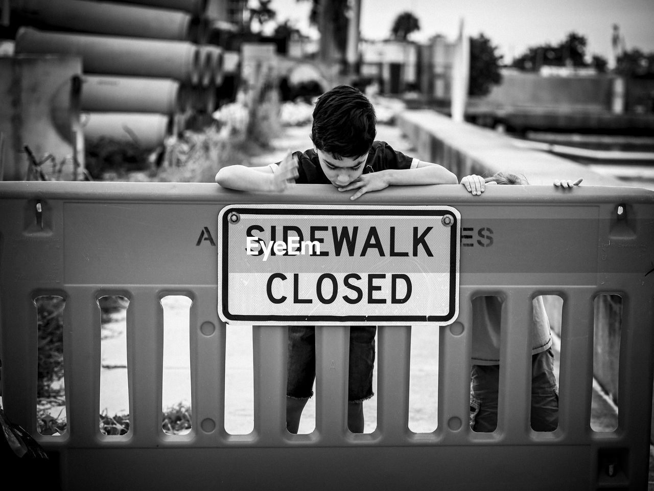 Boy standing behind sidewalk closed construction site sign