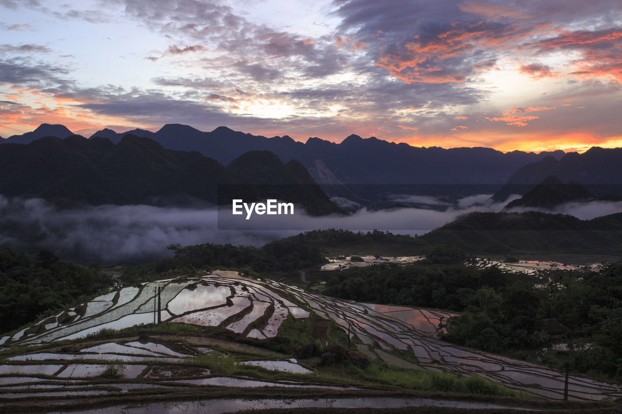 Terraced field by mountains against cloudy sky during sunrise