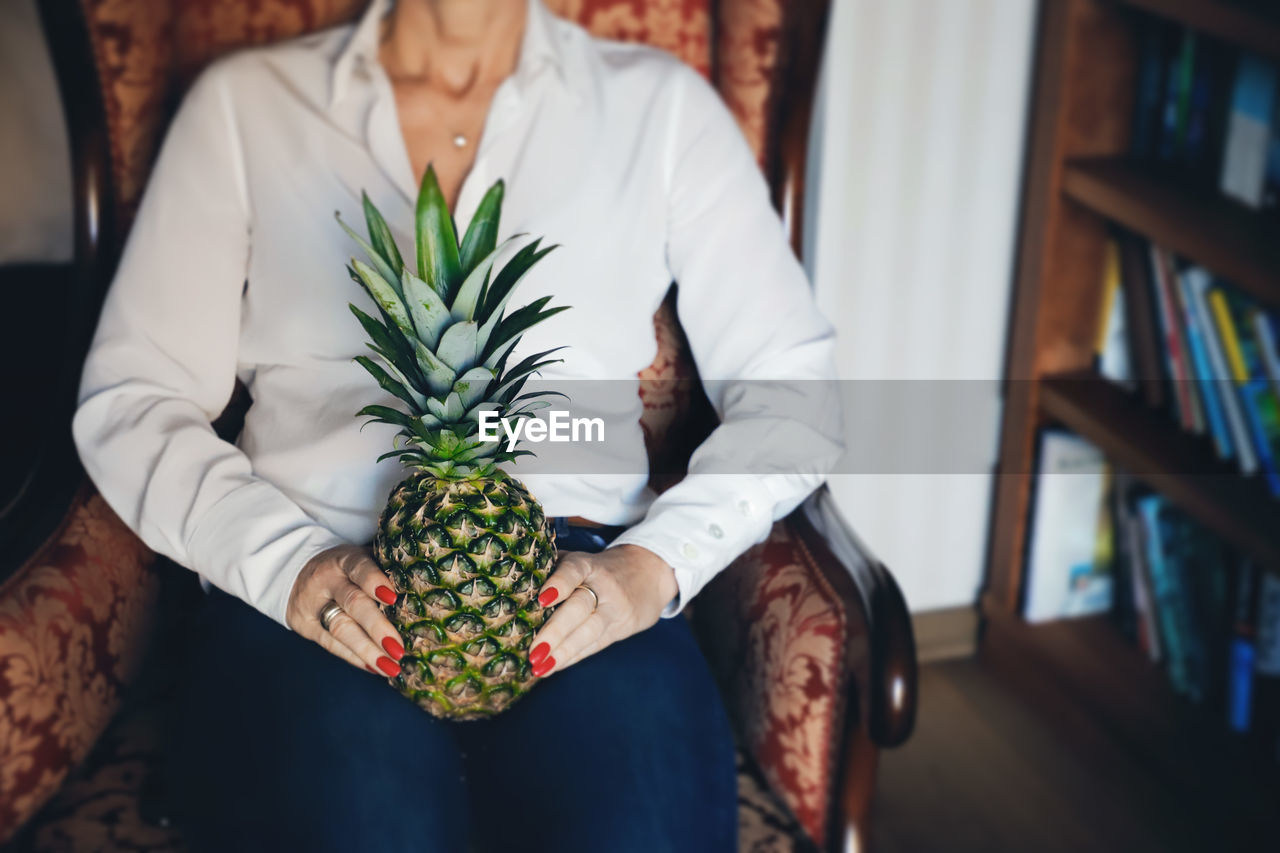 Midsection of woman holding pineapple at home