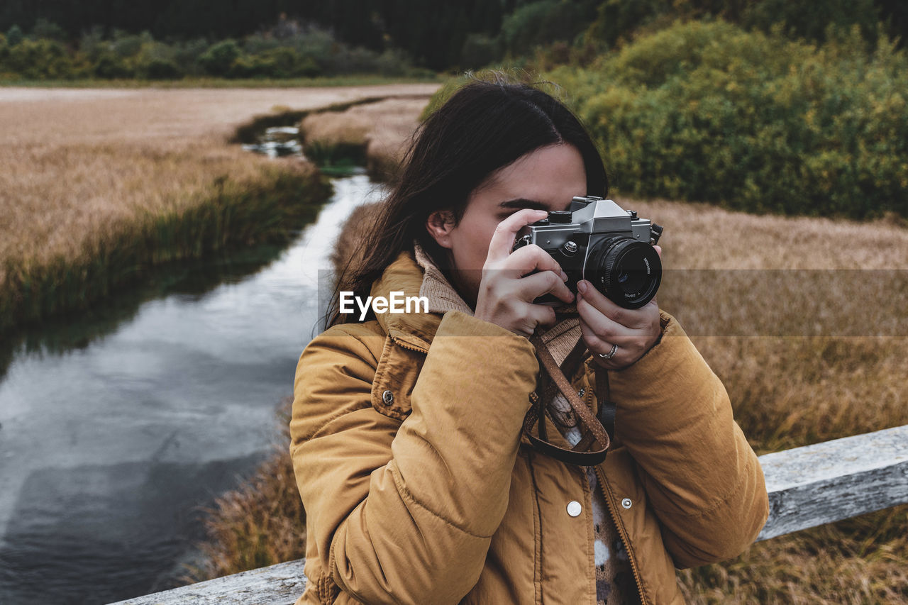 Portrait of young woman taking photos of autumn nature with vintage camera