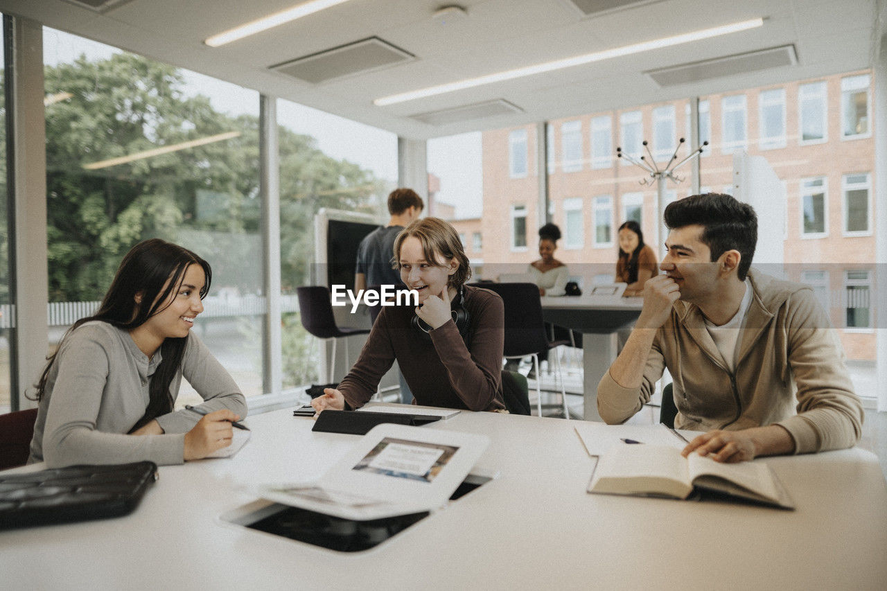 Happy multiracial male and female students studying at table in university