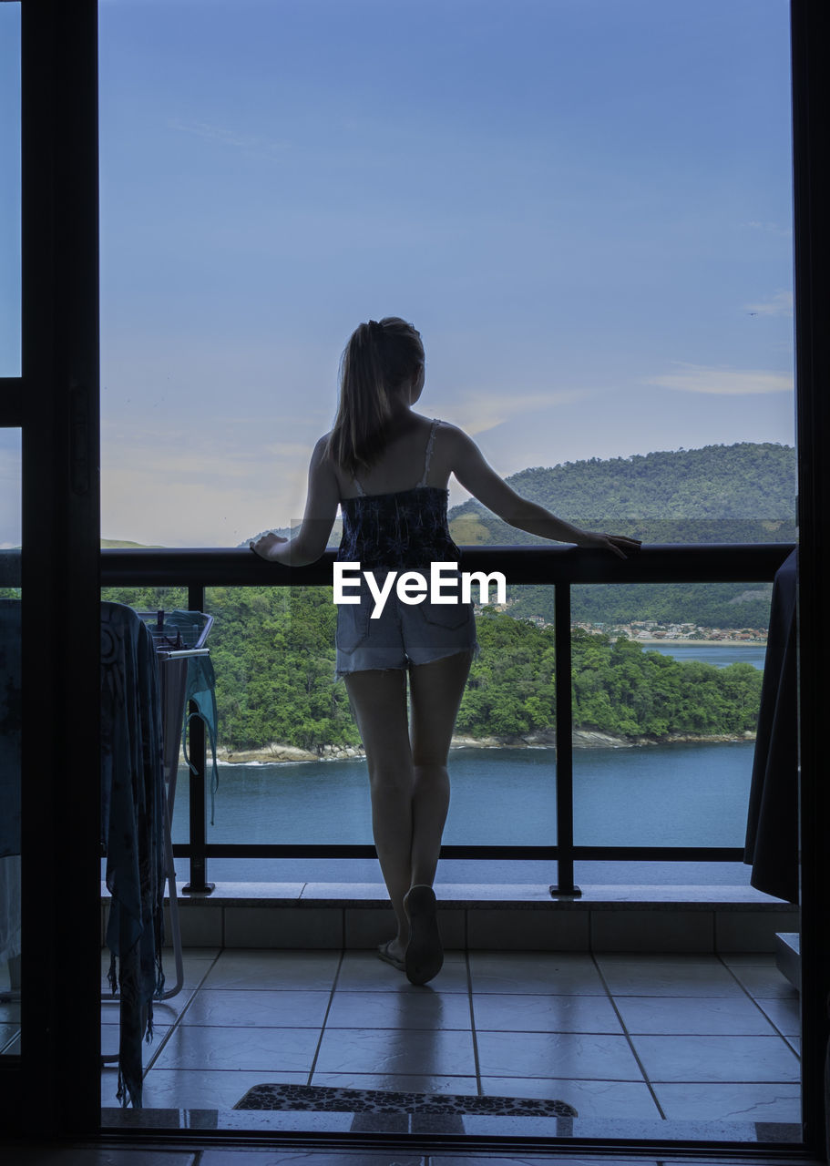 Rear view of woman standing at balcony against sky