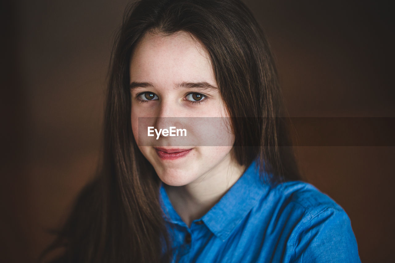 Close-up portrait of smiling girl against brown background