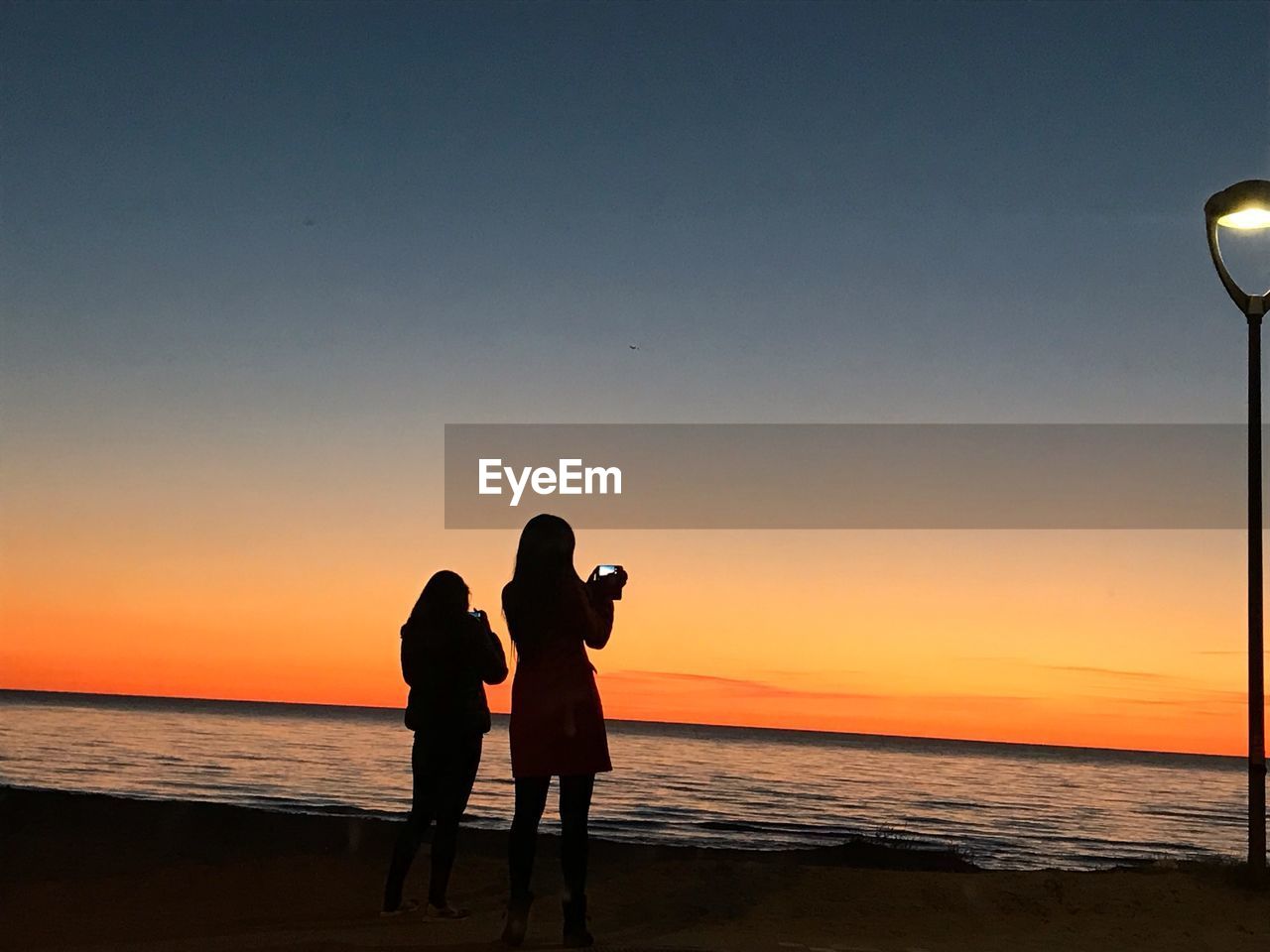 SILHOUETTE WOMEN STANDING AT BEACH DURING SUNSET