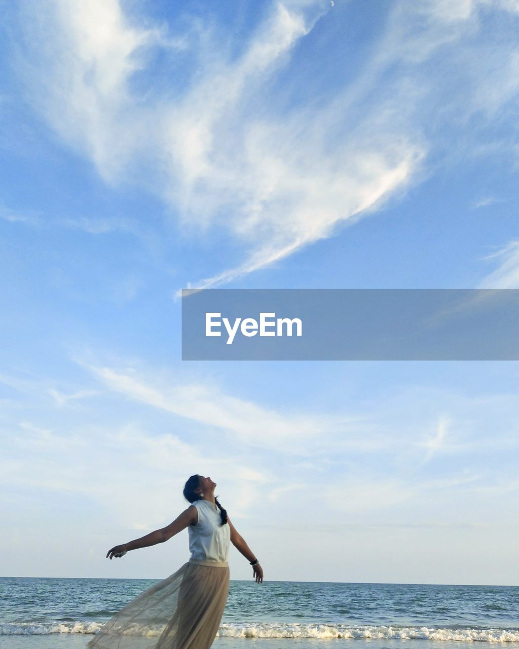 Woman with arms outstretched standing at beach against sky