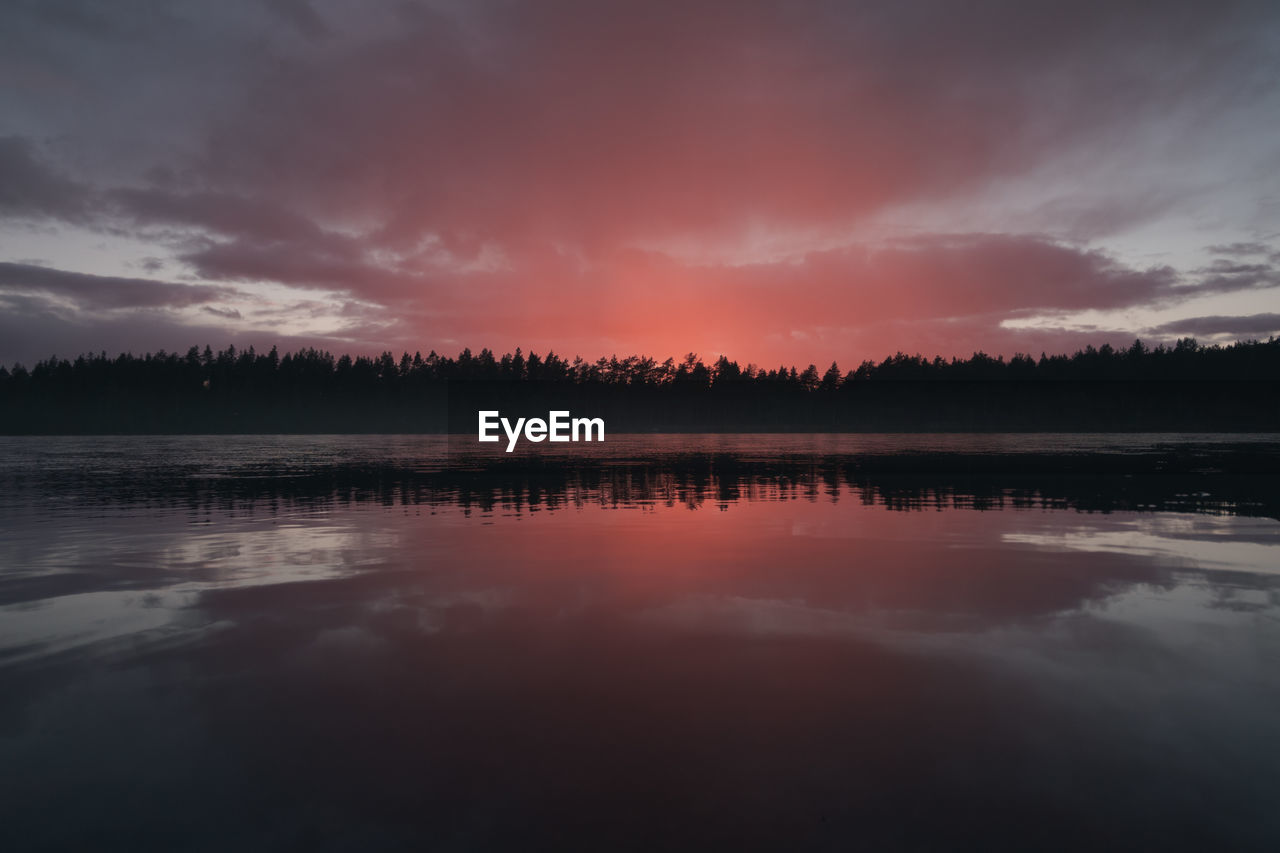 A cloud illuminated by the setting sun over a picturesque forest lake