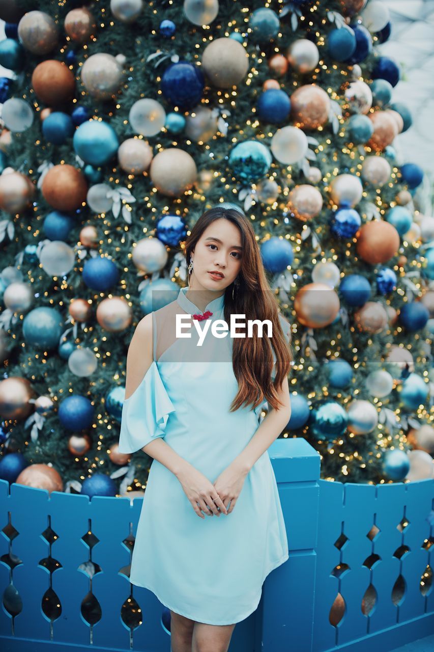 Portrait of smiling young woman standing by christmas tree outdoors