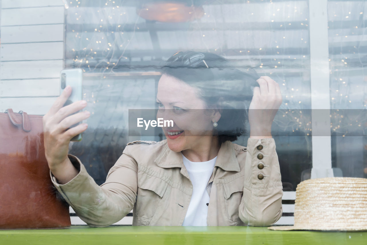 Young joyful woman talking on the phone by video link at a table in a cafe.