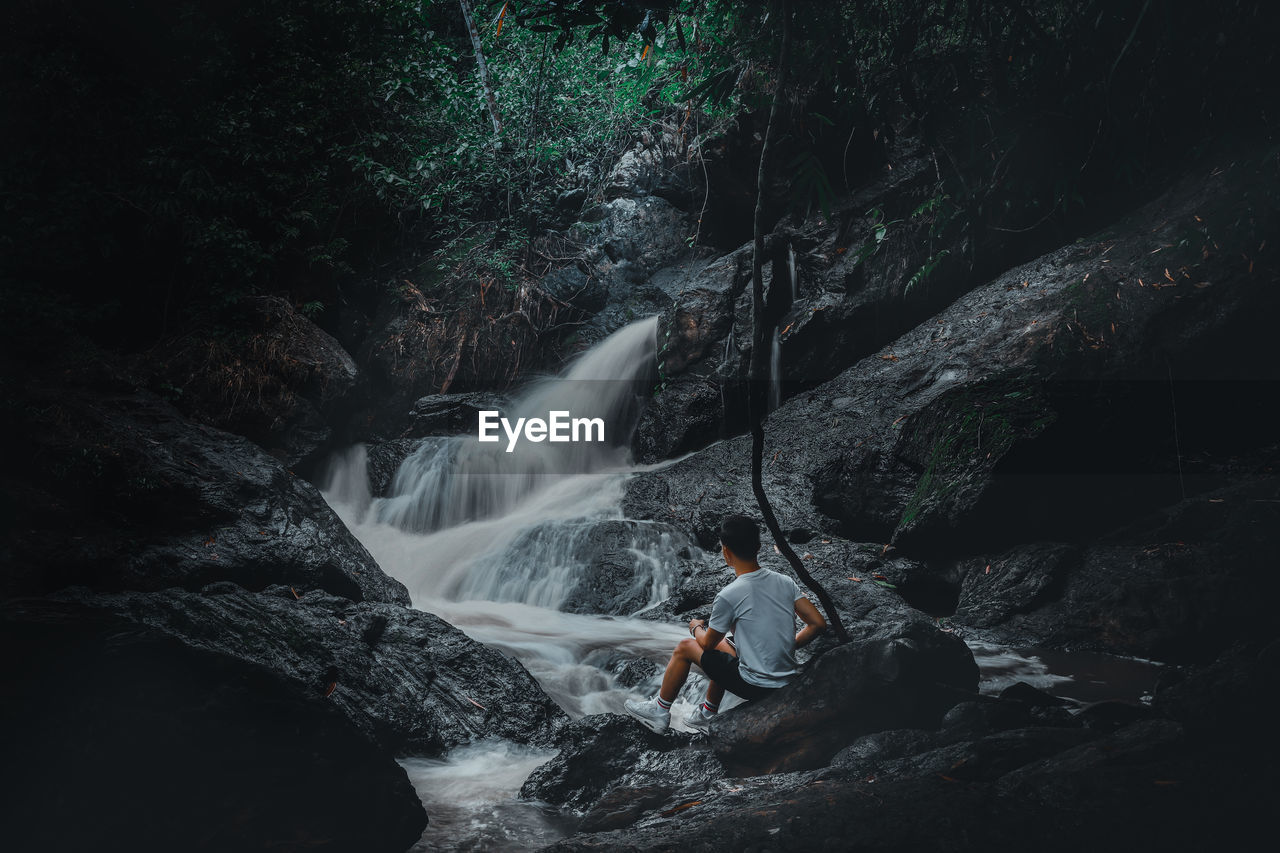 Man sitting on the rock looking at the waterfall background