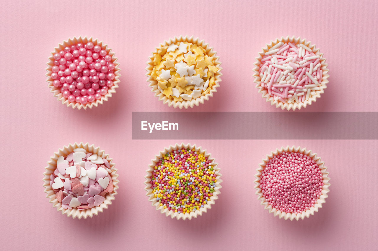 Directly above shot of colorful sprinkles in cups on pink background