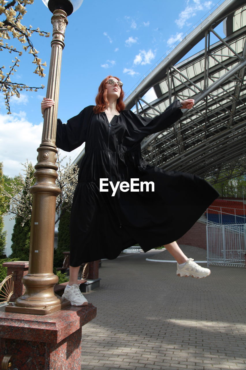 Full length of woman in oversized black dress walking to nowhere against built structure outdoors