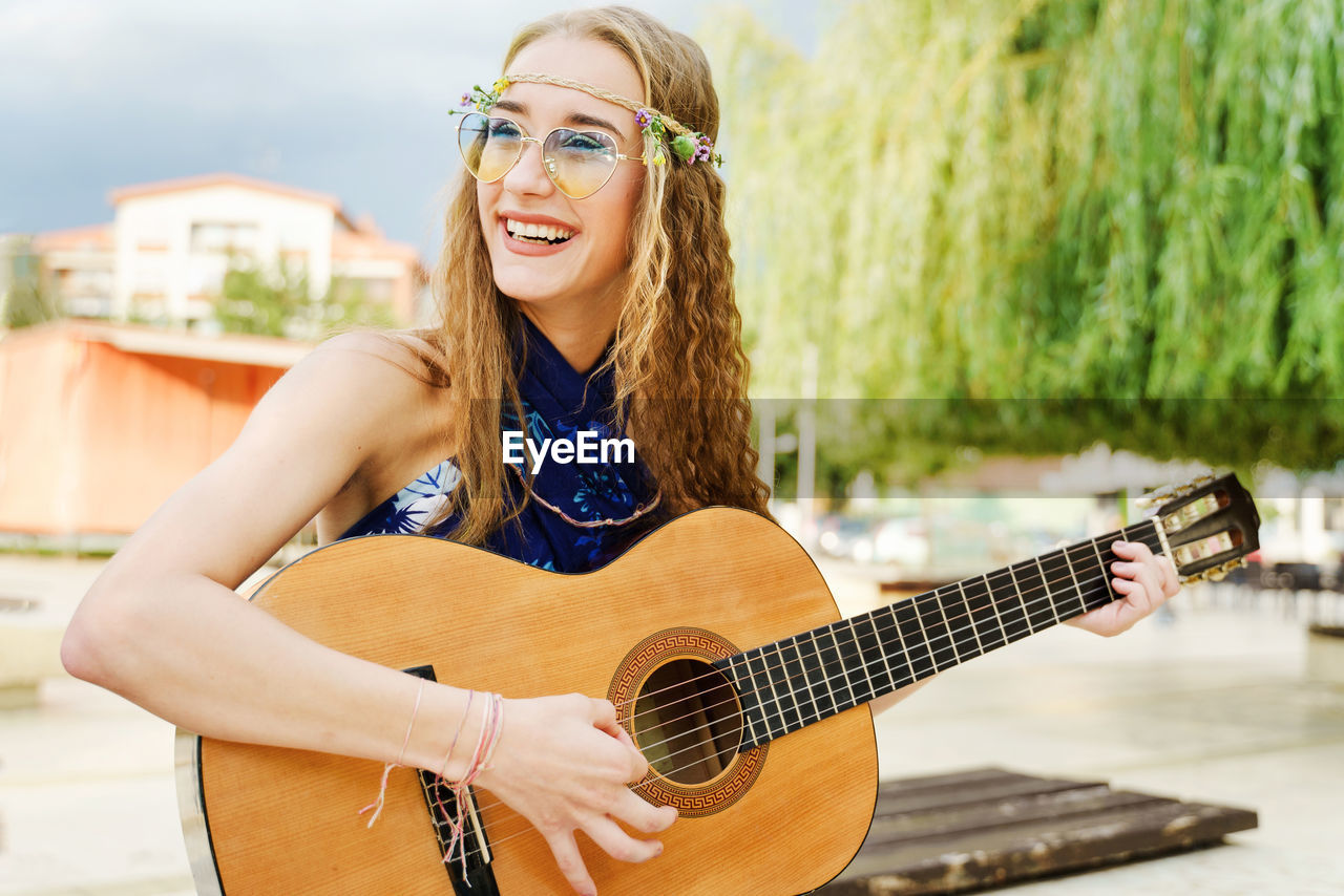 PORTRAIT OF YOUNG WOMAN PLAYING GUITAR OUTDOORS