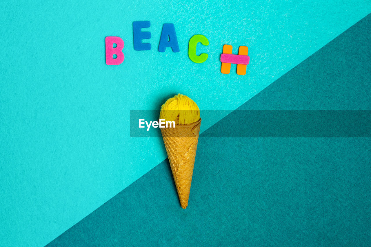 Overhead view of beach title over crunchy waffle cone with woolen thread ball on two color background