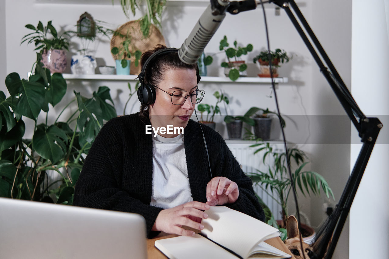 Woman doing podcast session while sitting against plant at home