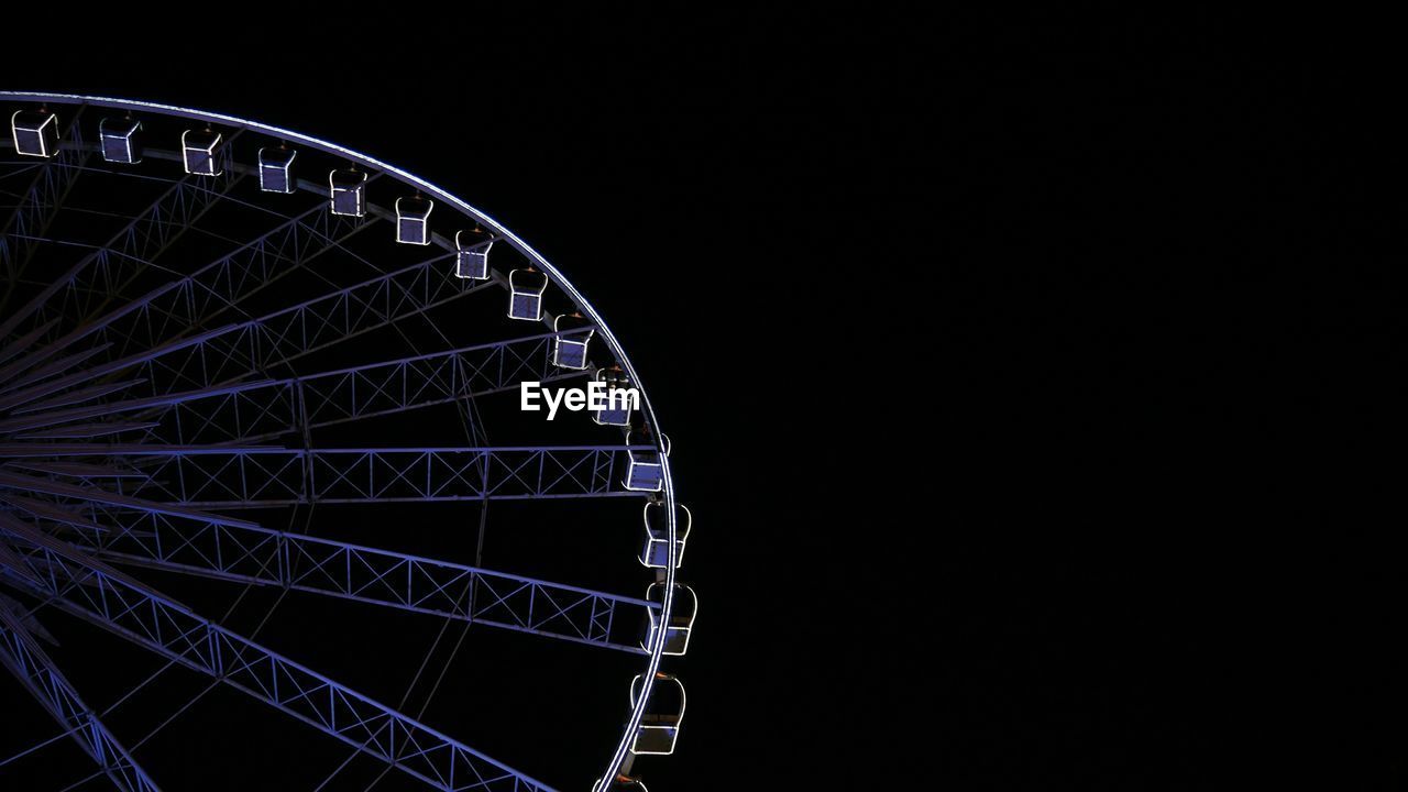 Low angle view of illuminated ferris wheel against clear sky at night