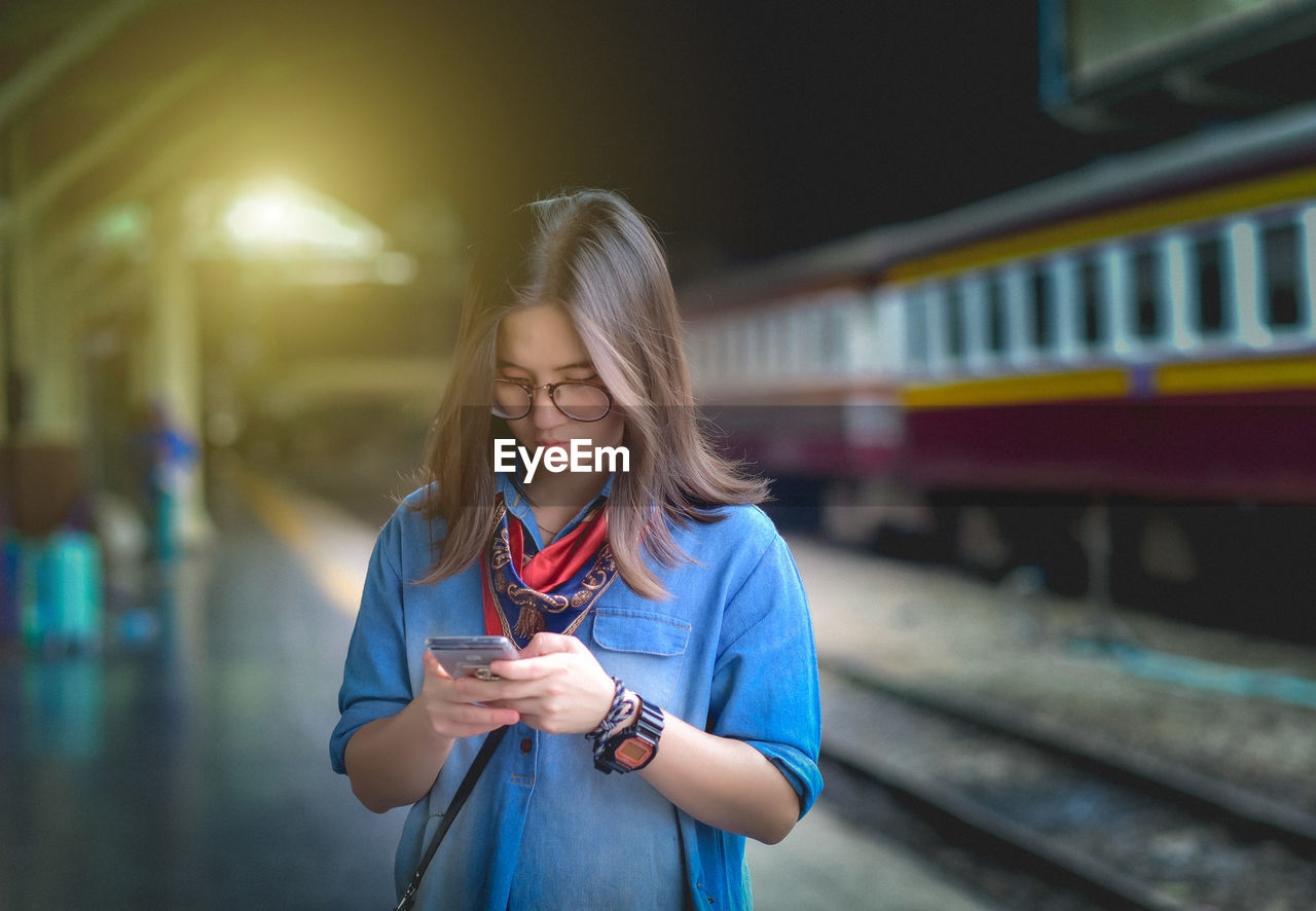 Woman using mobile phone while standing at railroad station platform