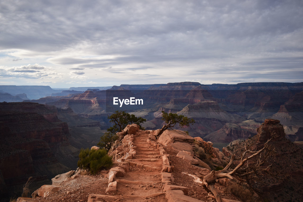 Scenic view of mountain pathway leading to center of frame-  cloudy sky in background.