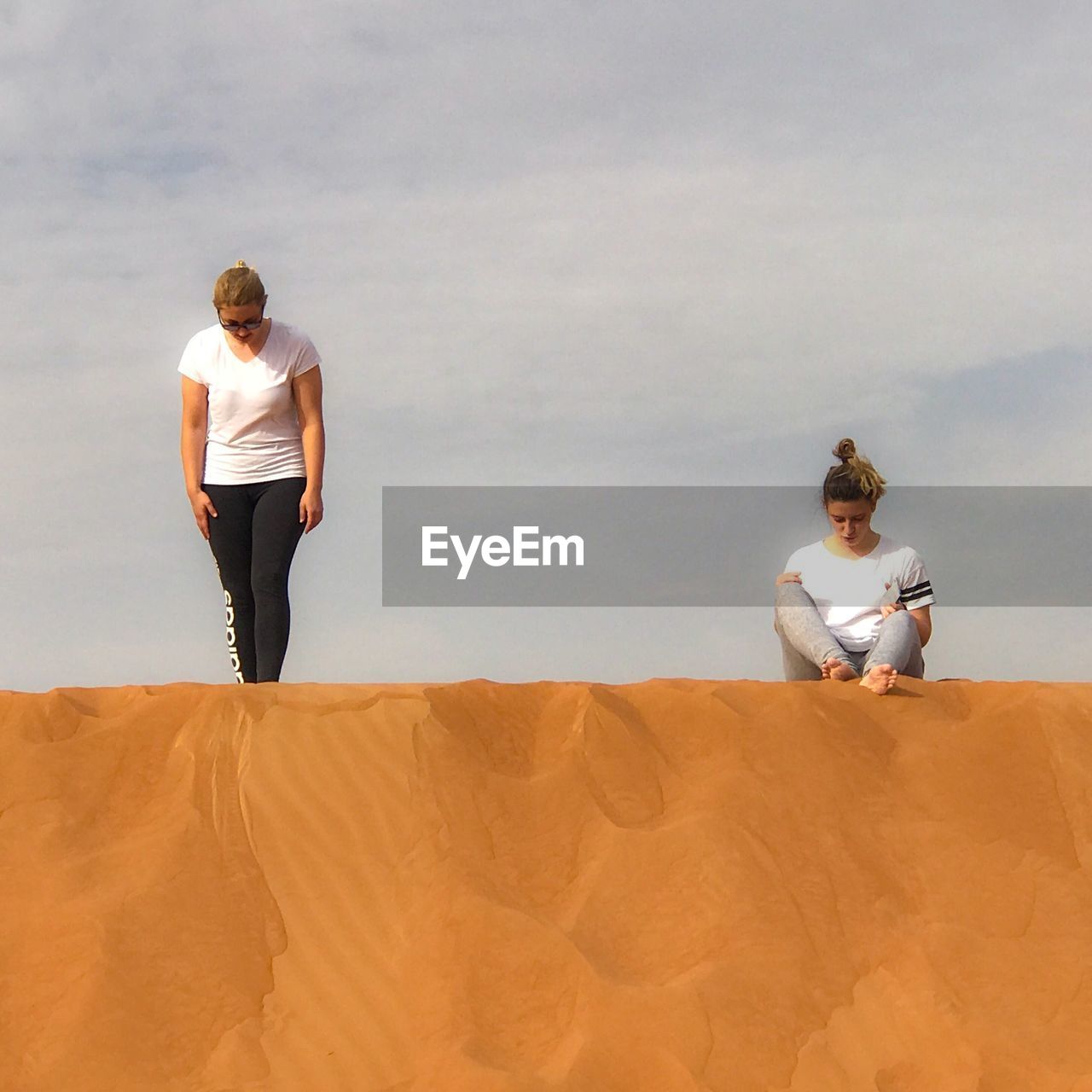 Friends on sand against sky during sunny day