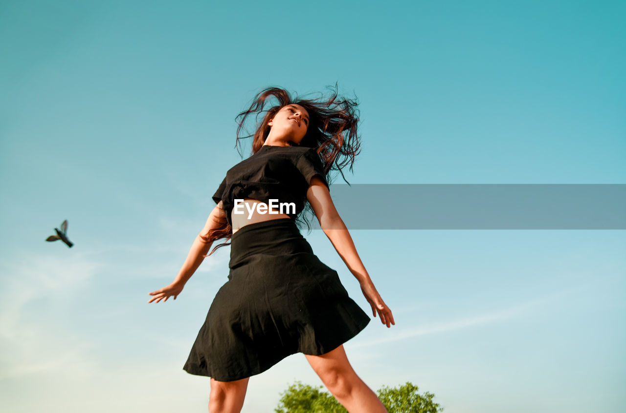 Low angle view of young woman dancing against blue sky