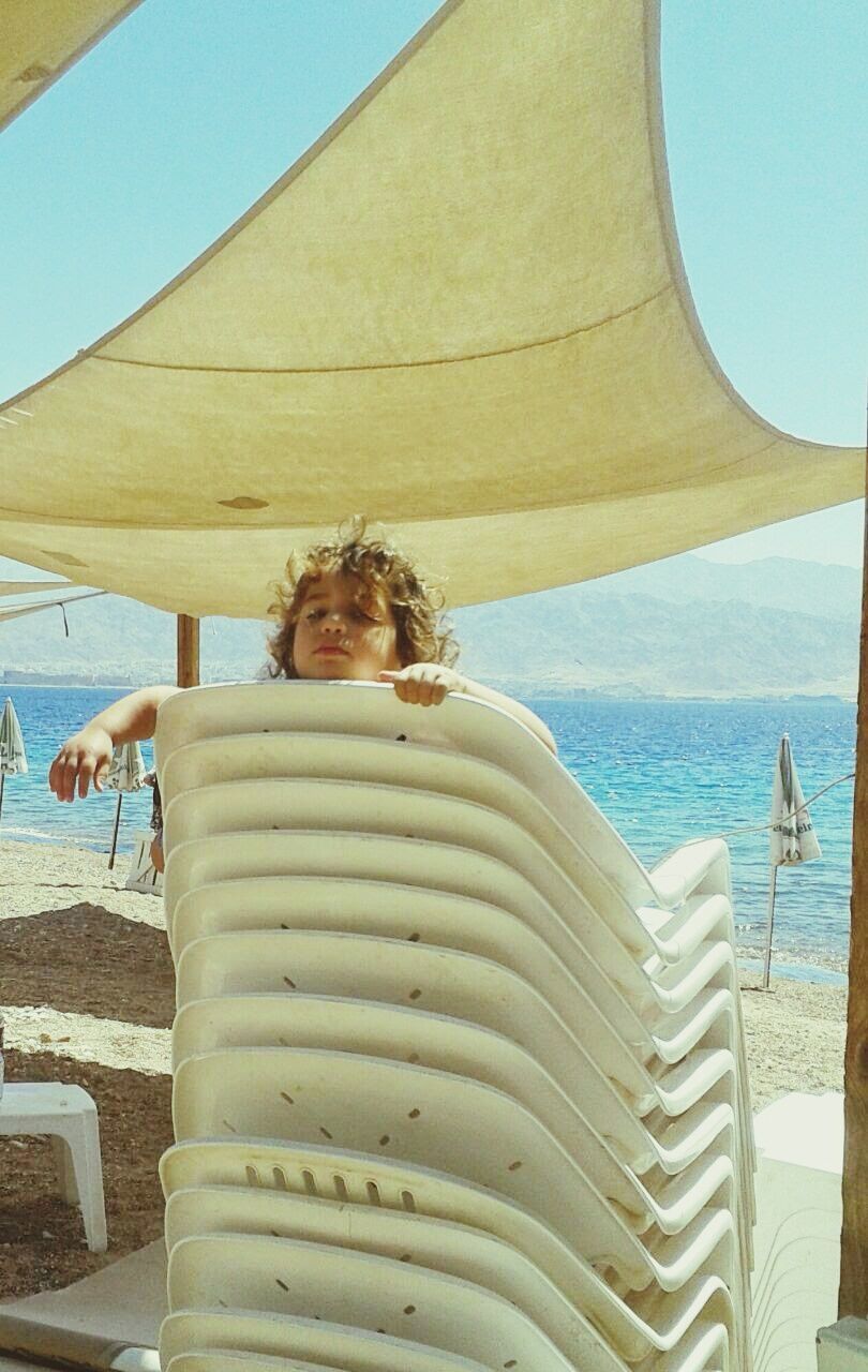 Cute girl on stack on chair at beach during sunny day