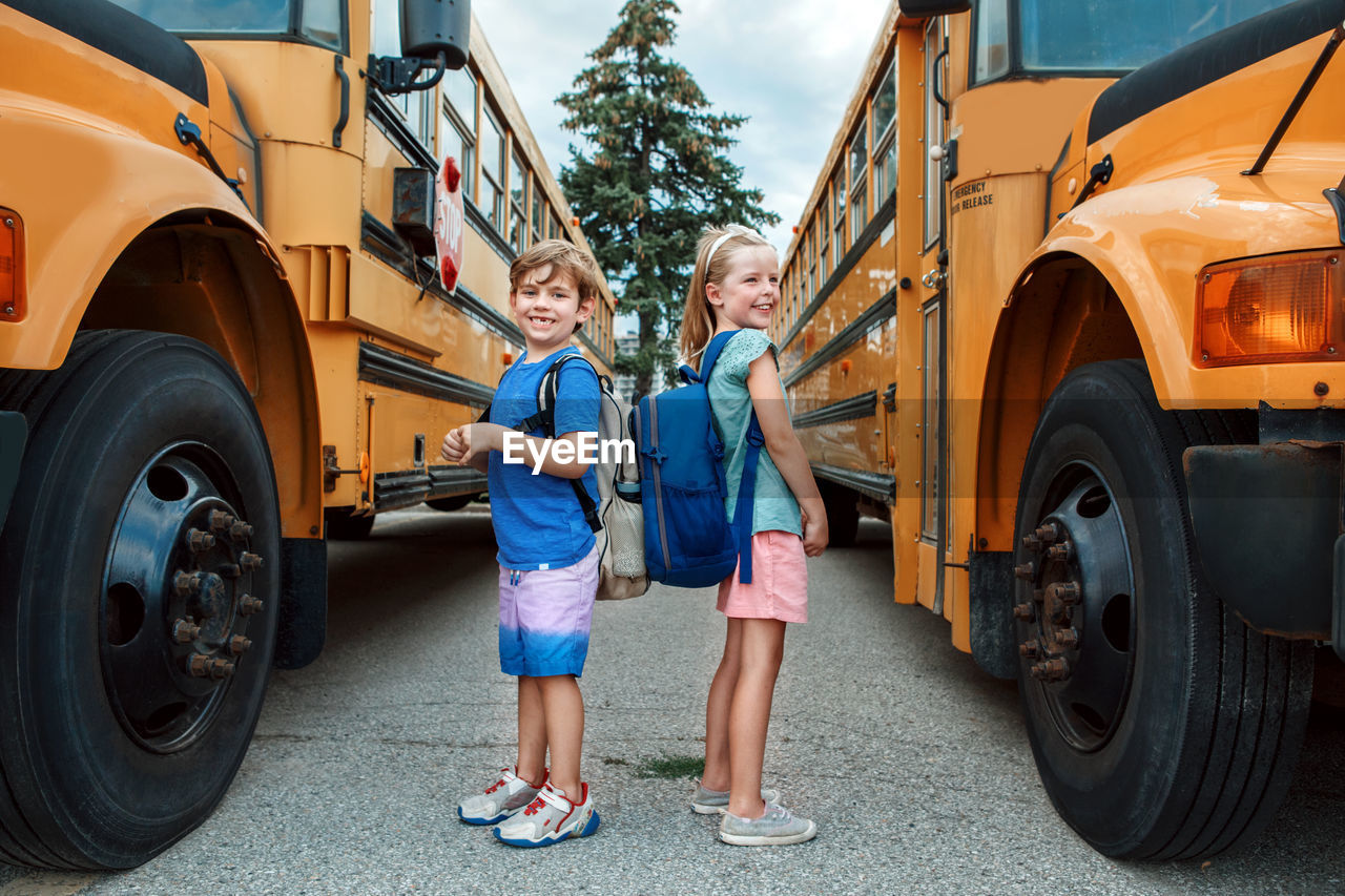 Happy caucasian children boy and girl kids students standing by yellow school bus. education 