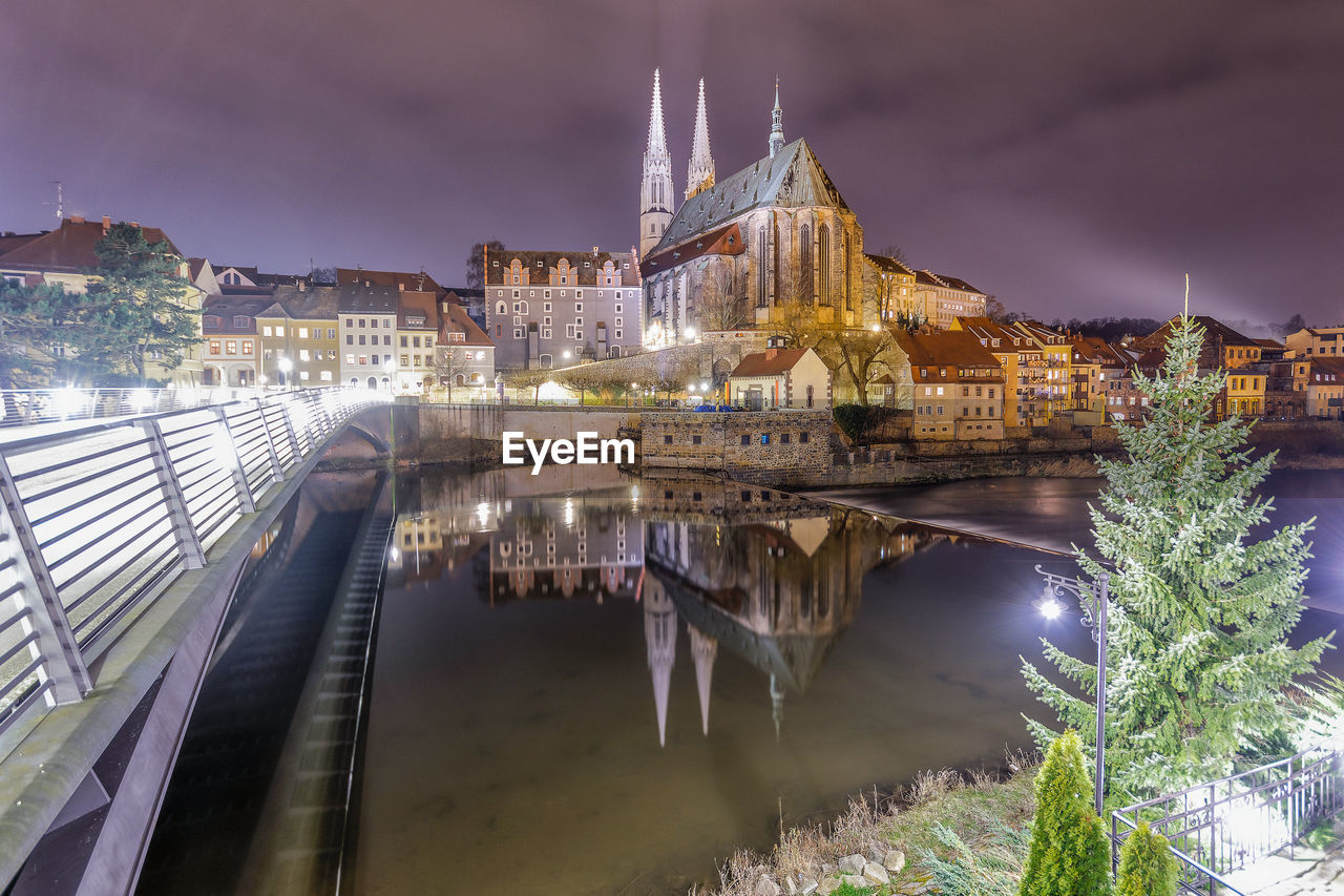 Illuminated buildings by river against sky in city at night