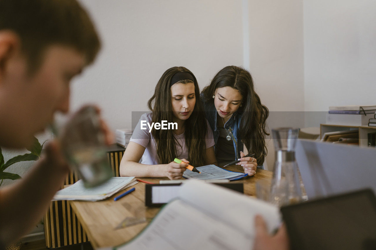 Young female friends reading while studying together at table