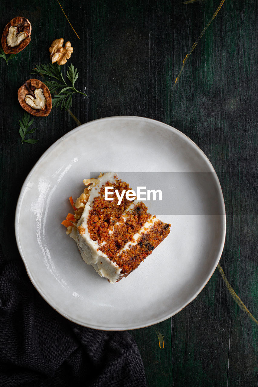 Top view of yummy cake with cream cheese served on plate with fresh carrot slices and walnuts