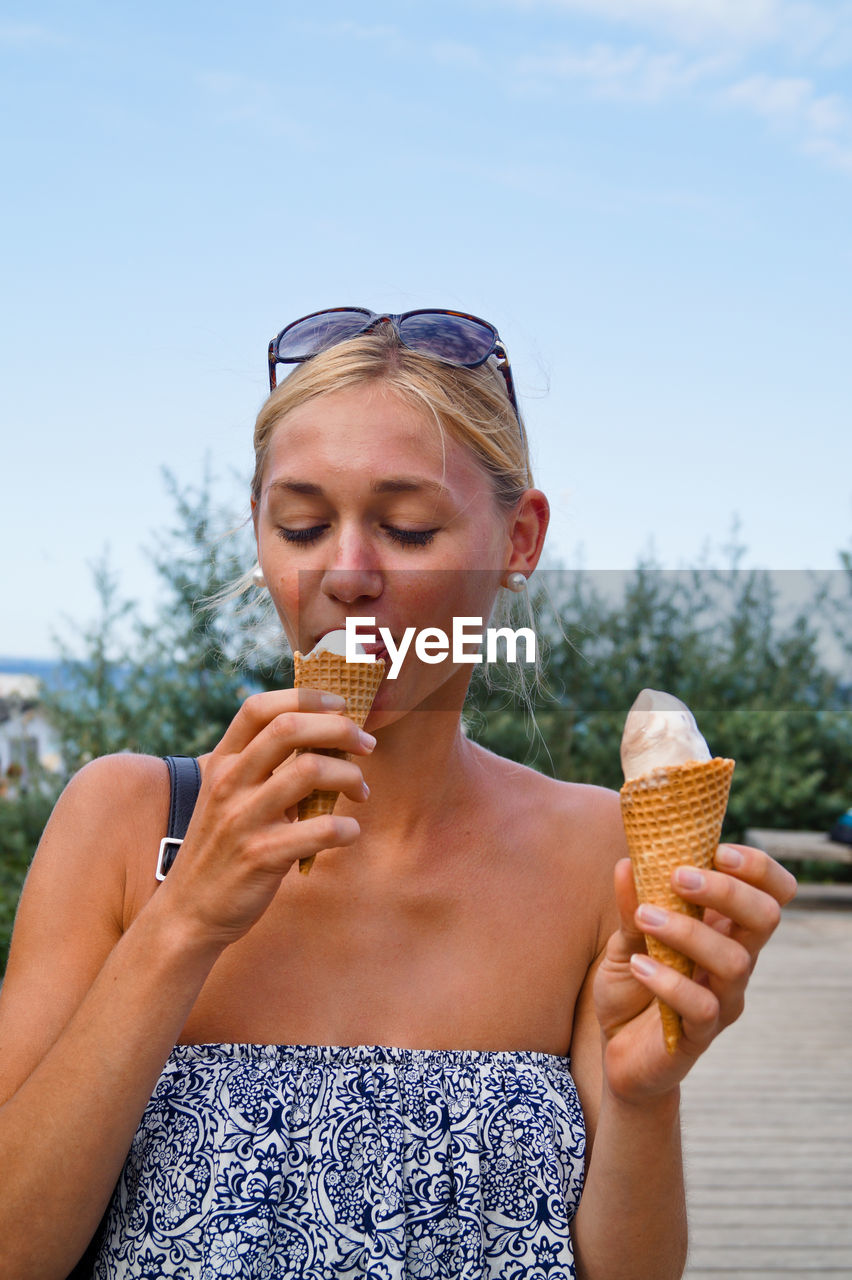 Woman licking ice cream on street against sky