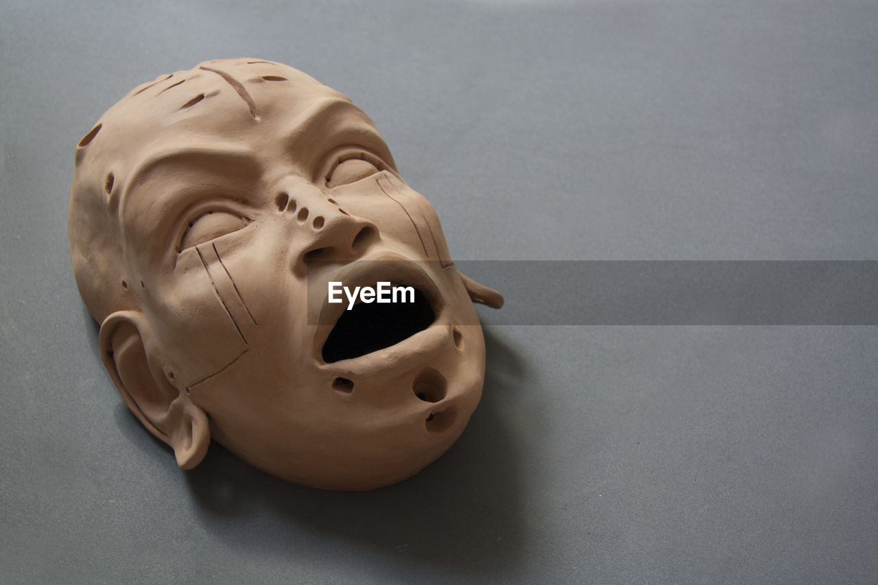 Sculpture of the face in clay. female mask with open mouth on a grey floor. dark and gothic art. 