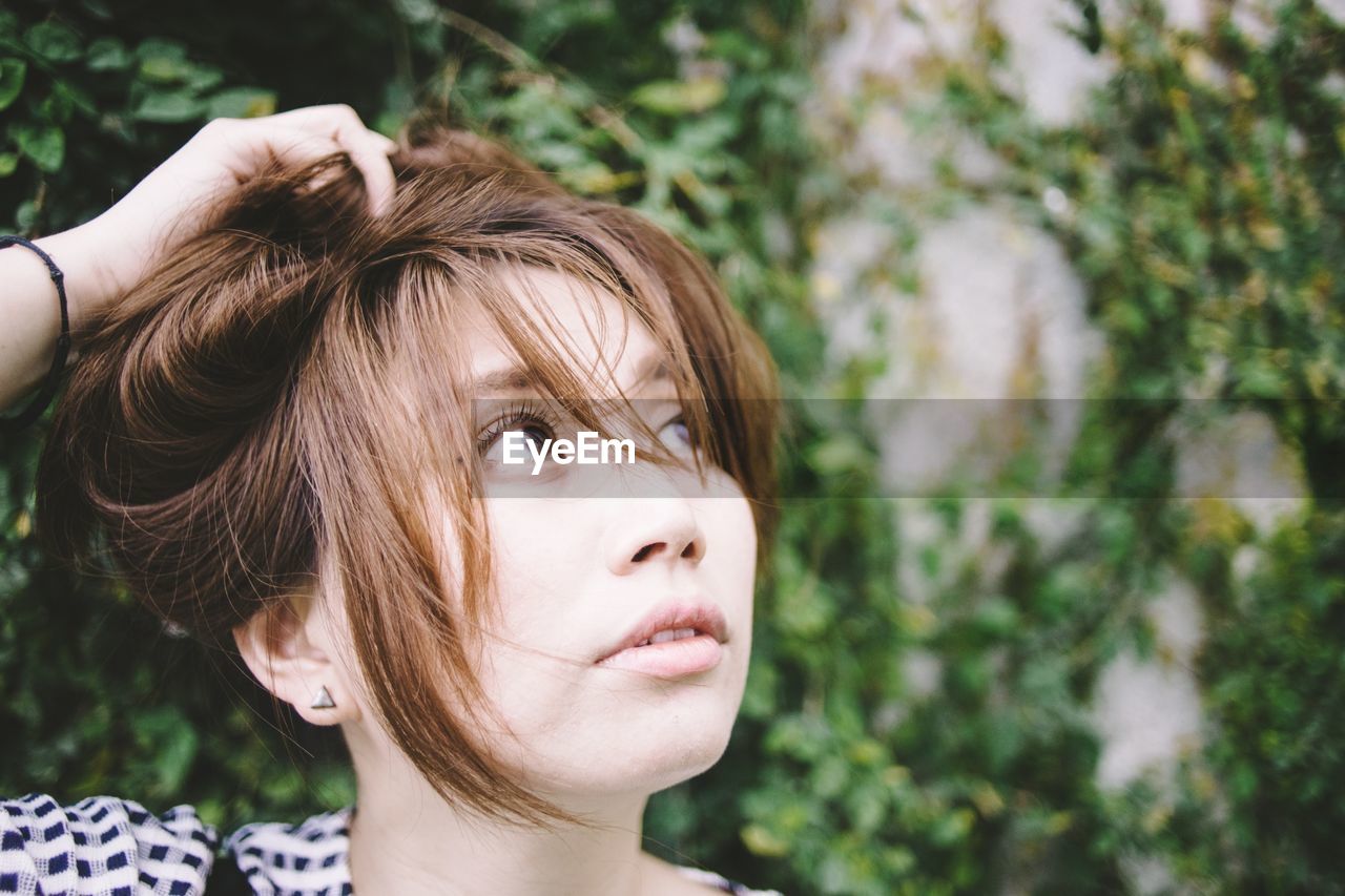 Close-up of woman looking away against creeper on wall