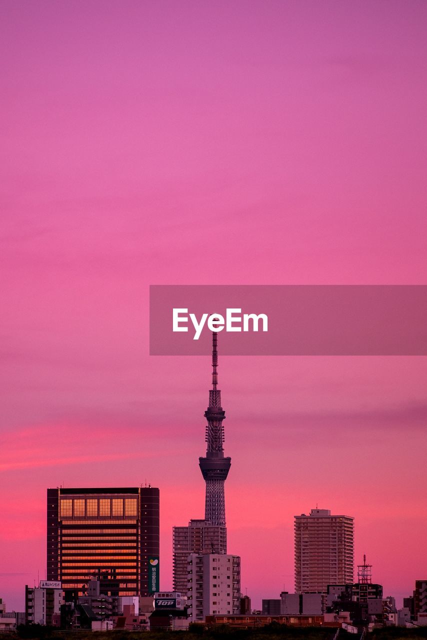 Buildings in city against romantic sky at sunset