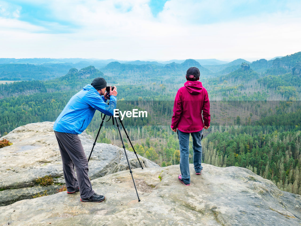 Photographer check viewfinder of camera on tripod and framing natural scene with woman hiking model 