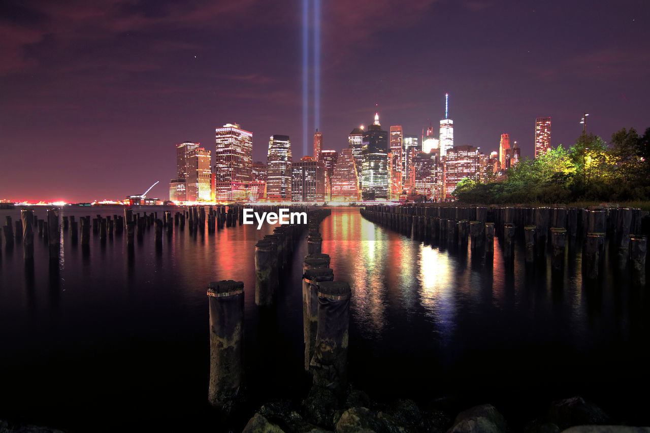 Wooden posts on east river against world trade center in city at night