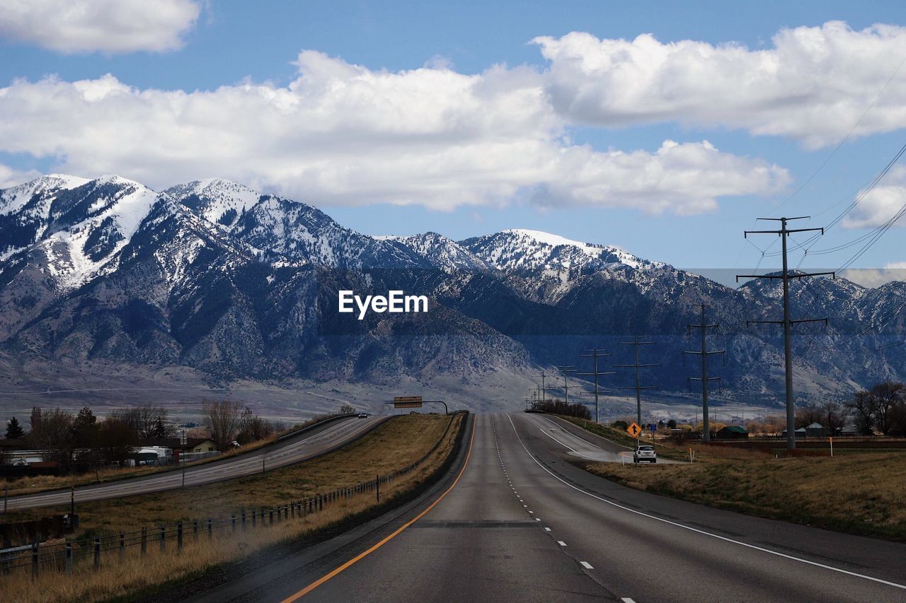 Road leading towards snowcapped mountains against sky