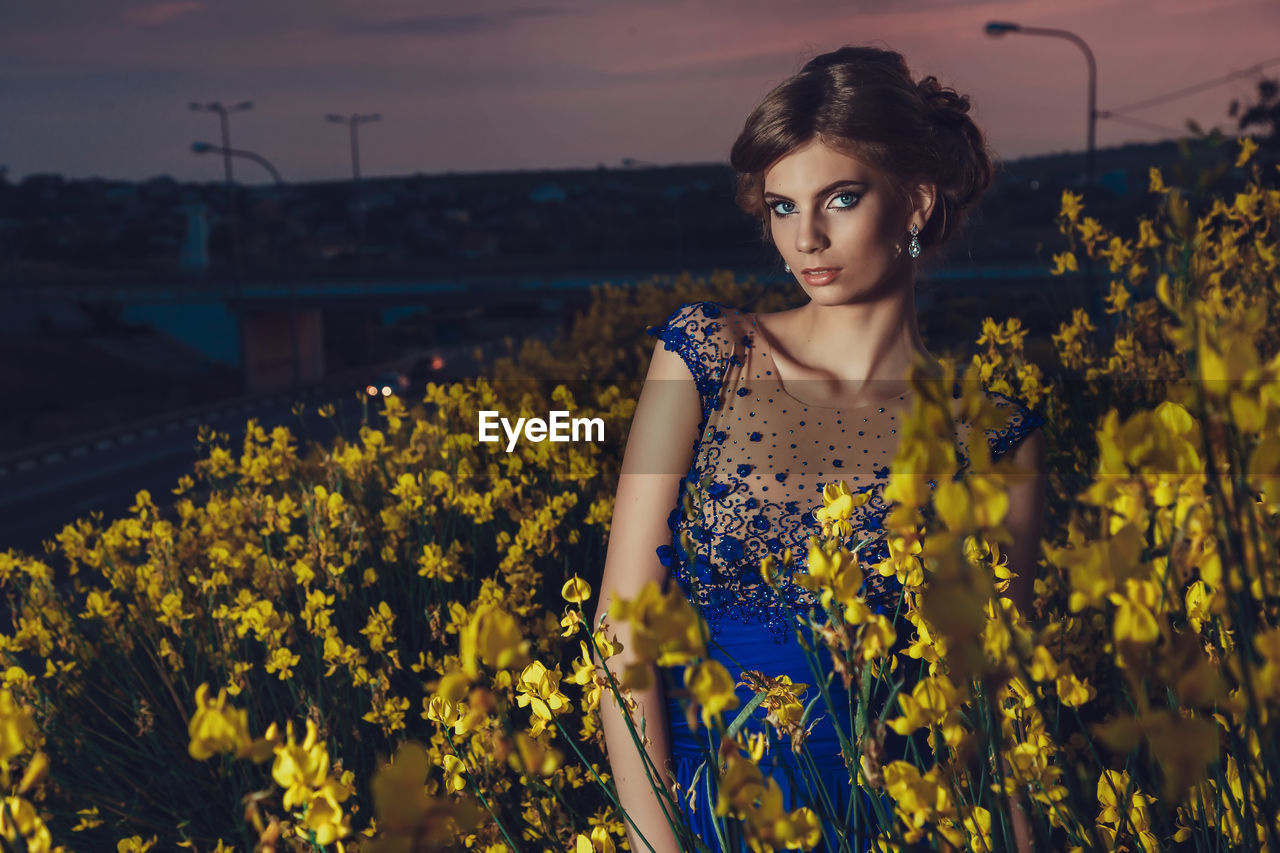 Beautiful young woman standing in the yellow flowers at summer sunset