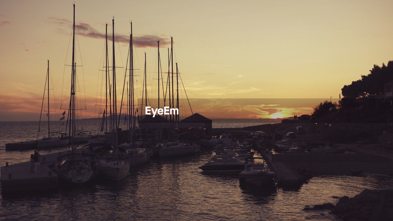 Boats moored at harbor against sky during sunset